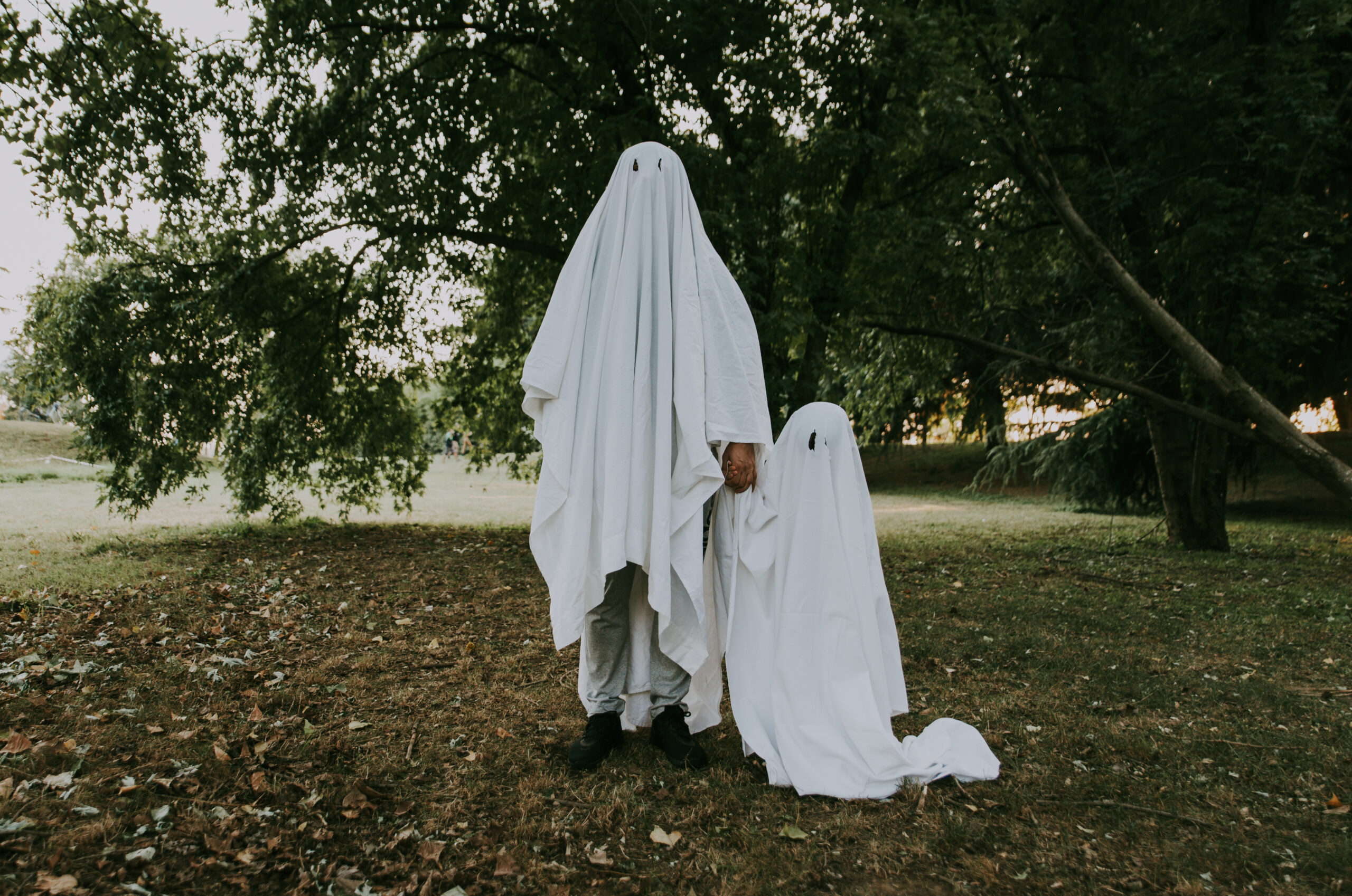 Father and son playing ghosts with white sheets in the garden, conceptual photos about halloween holidays