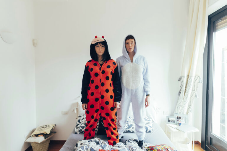 Portrait of women wearing adult bodysuit standing on bed looking at camera