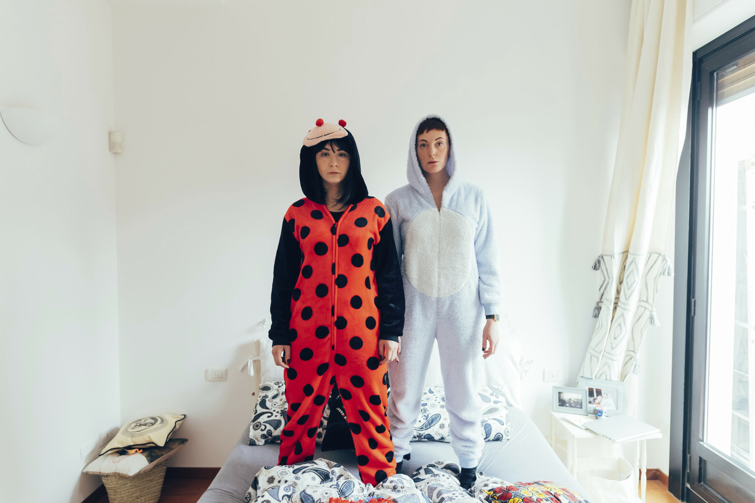 Portrait of women wearing adult bodysuit standing on bed looking at camera