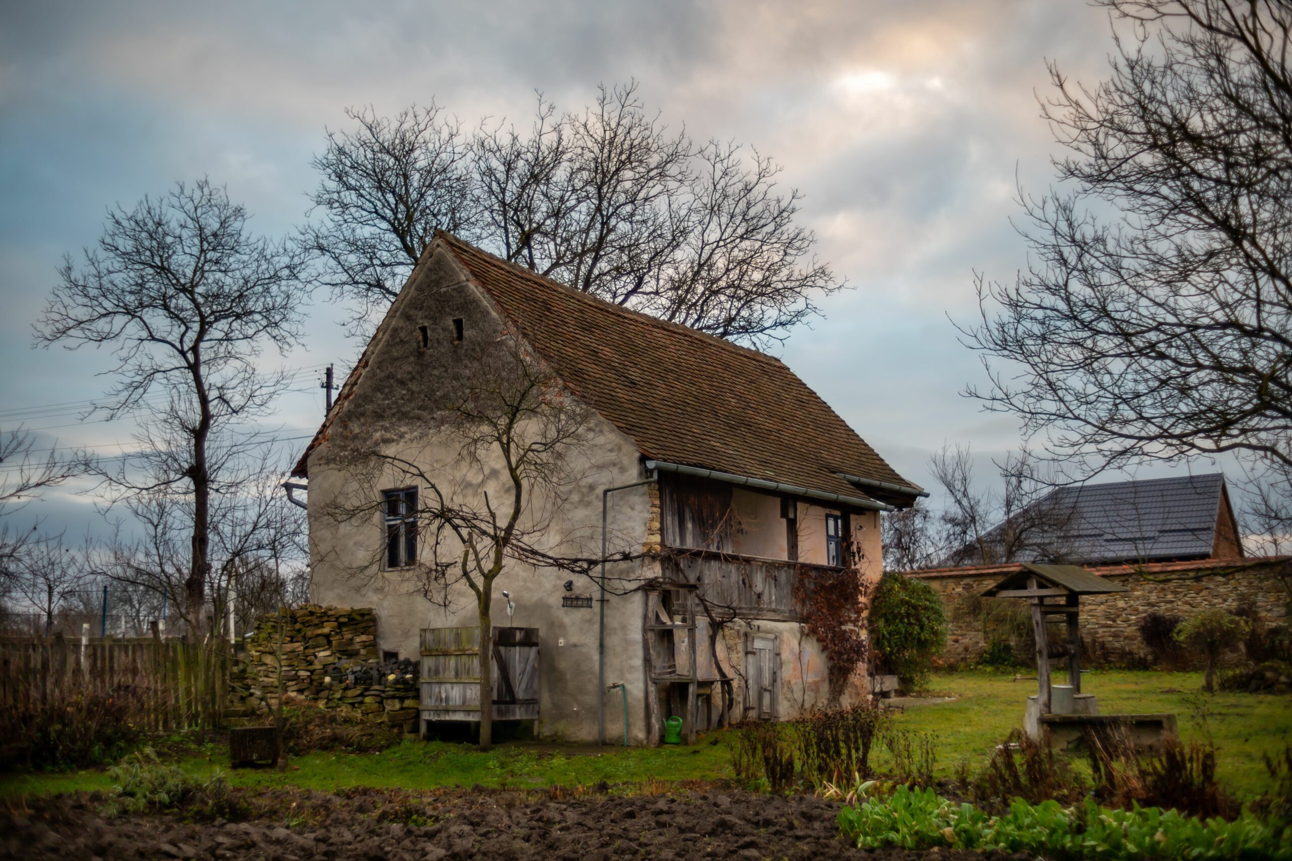 A scenic view of an old rural house with a green lawn and bare trees on a cloudy day
