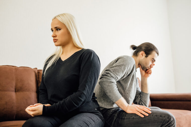 Stubborn angry husband and wife, spouses sit separate on sofa at home ignore each other avoid talking after arguing. Unhappy young Caucasian couple think of divorce breakup after family quarrel.