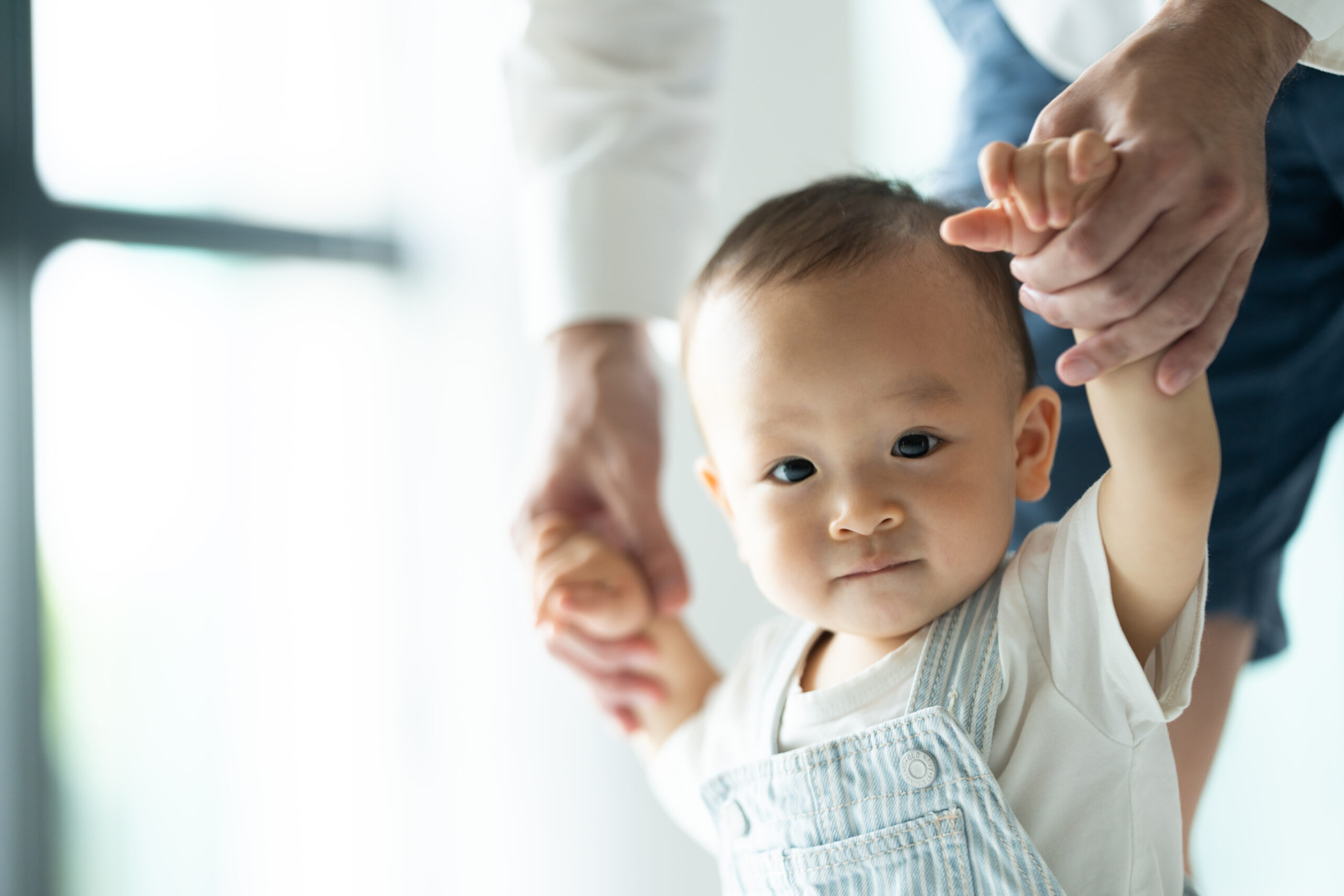 toddler baby learning to walk and having support by family together, little child with father and mother at home with first step to walking by help and holding hand from dad, happy childhood help care